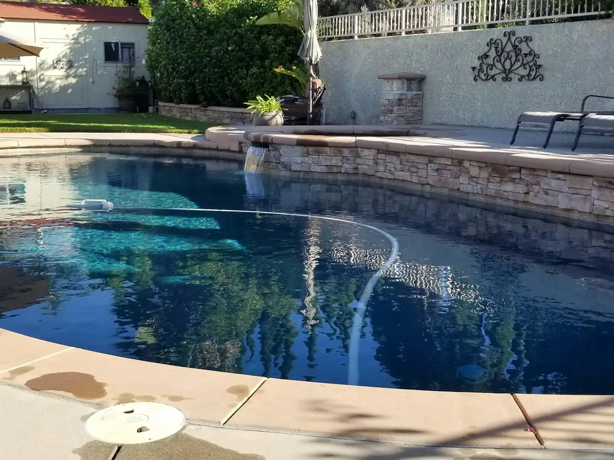 A backyard swimming pool with a stone edge and lounge chairs