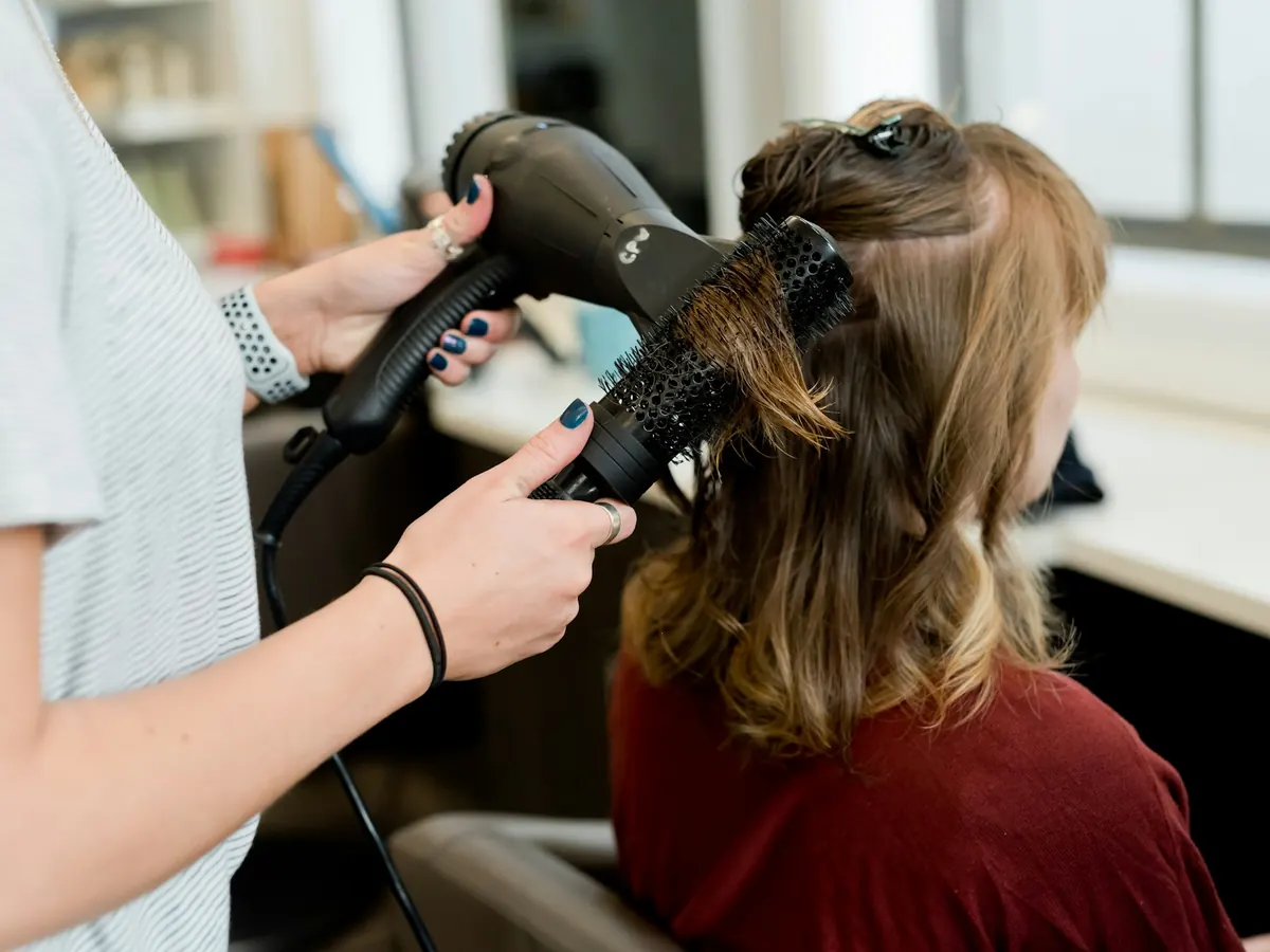 A stylist blow-drying a client's hair with a round brush